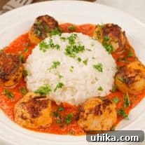 A plate of paprika-crusted, pan-seared sea scallops in roasted red pepper sauce arranged around a serving of white rice, all garnished with chopped parsley.