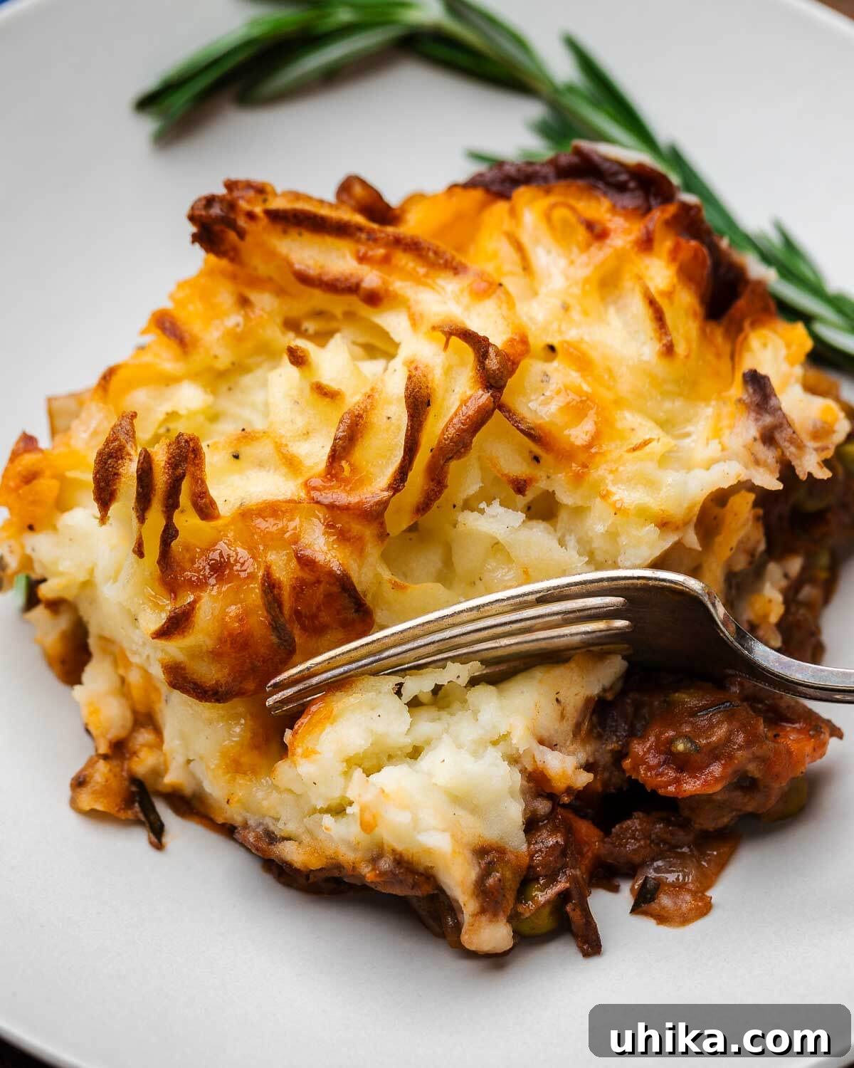 Slow-Braised Short Rib Cottage Pie 4 Close-up shot of a fork scooping a piece of Cottage Pie from a white plate, showing layers of mashed potato, beef, carrots, and peas.