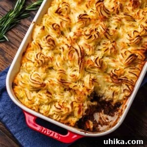 Cottage pie in red baking dish with a piece removed, highlighting the layers of beef and mashed potatoes.