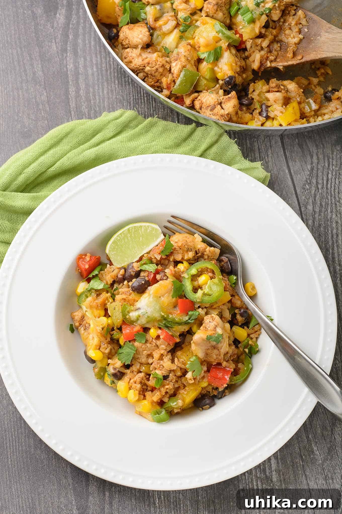 Fiesta Chicken Cauli Rice 3 A beautifully plated serving of Southwest chicken and cauliflower rice, presented in a shallow bowl and garnished with a fresh lime wedge and a vibrant jalapeno slice. The main skillet is visible in the background.