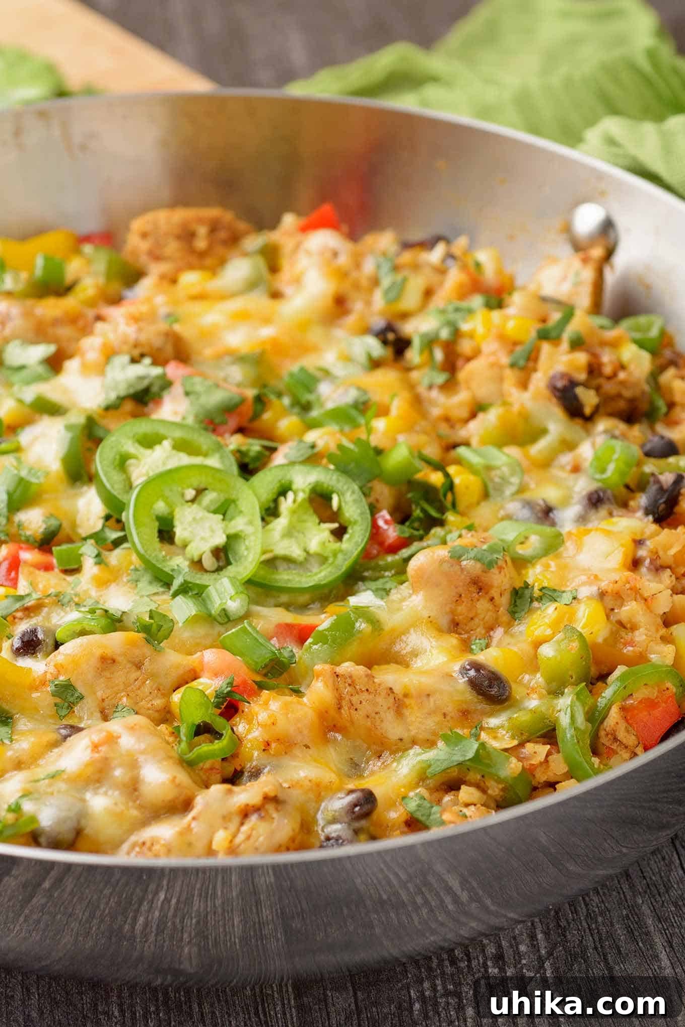 Fiesta Chicken Cauli Rice 4 A close-up shot of Southwest-style chicken and cauliflower rice generously topped with melted Mexican-style cheese, garnished with vibrant green onions, finely chopped cilantro, and thin slices of jalapeño.