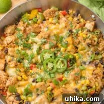 A frying pan filled with Southwest-style chicken and cauliflower rice with bell peppers, corn, scallions, beans, garnished with sliced jalapenos and cilantro.
