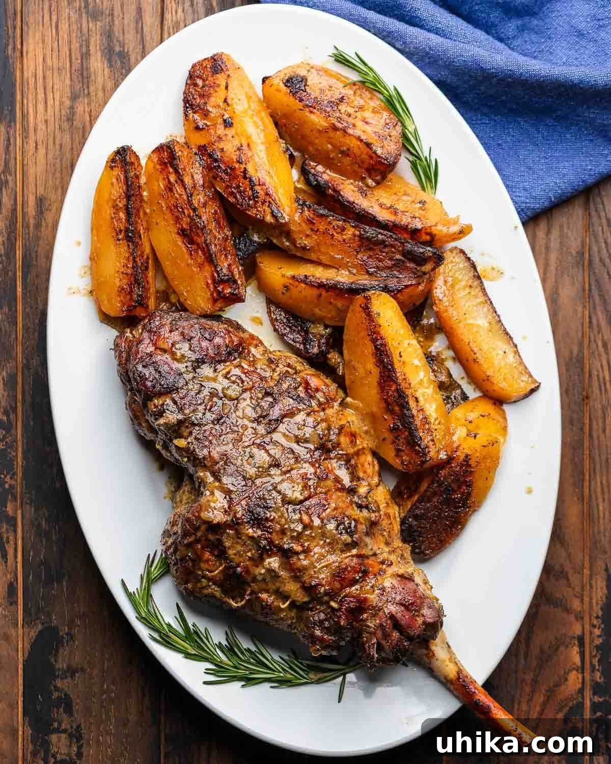 Succulent Greek Slow-Roasted Lamb Leg with Lemon-Herb Potatoes 2 Large white platter with perfectly cooked Greek-style bone-in leg of lamb surrounded by golden brown potato wedges, garnished with fresh herbs.