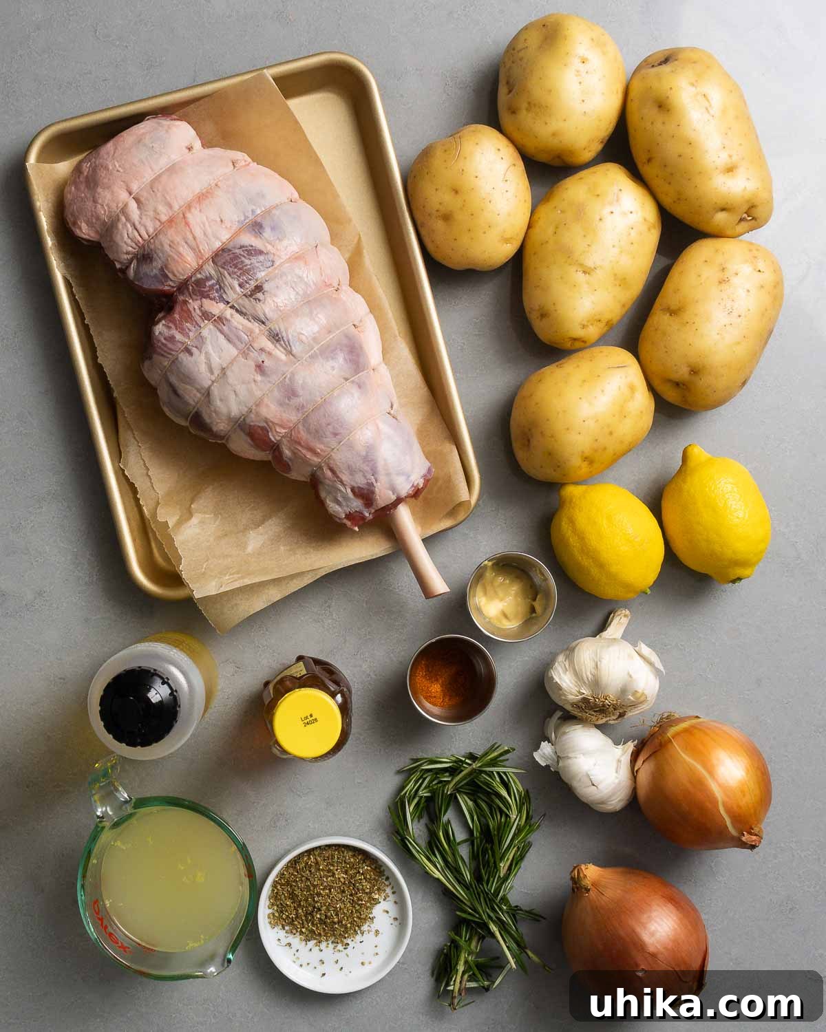 Succulent Greek Slow-Roasted Lamb Leg with Lemon-Herb Potatoes 3 A flat lay photograph showcasing all the ingredients for Greek leg of lamb: bone-in lamb leg, Yukon Gold potatoes, fresh lemons, garlic cloves, fresh rosemary, dried Greek oregano, olive oil, honey, Dijon mustard, paprika, and chicken stock.