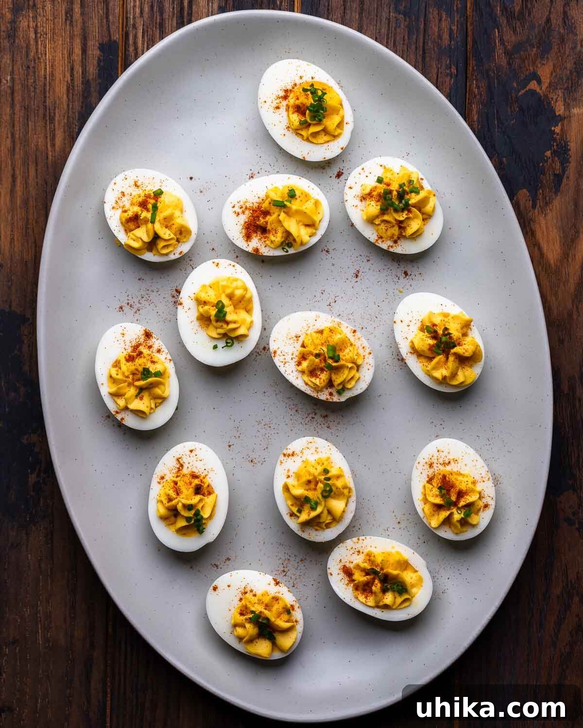 Timeless Deviled Eggs 2 A large, beautifully arranged platter filled with classic deviled eggs, garnished with a sprinkle of paprika and fresh chives, sitting on a rustic wooden table.