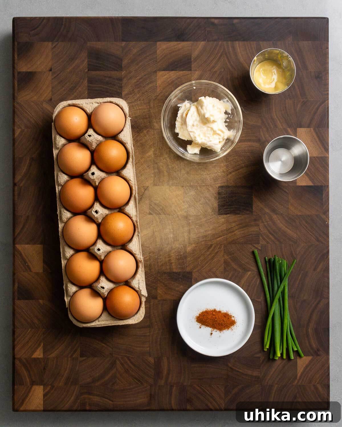 Timeless Deviled Eggs 3 A flat lay photograph showcasing all the ingredients required for classic deviled eggs: a carton of a dozen large eggs, a jar of mayonnaise, a bottle of Dijon mustard, a bottle of white vinegar, a shaker of paprika, and a bunch of fresh chives.