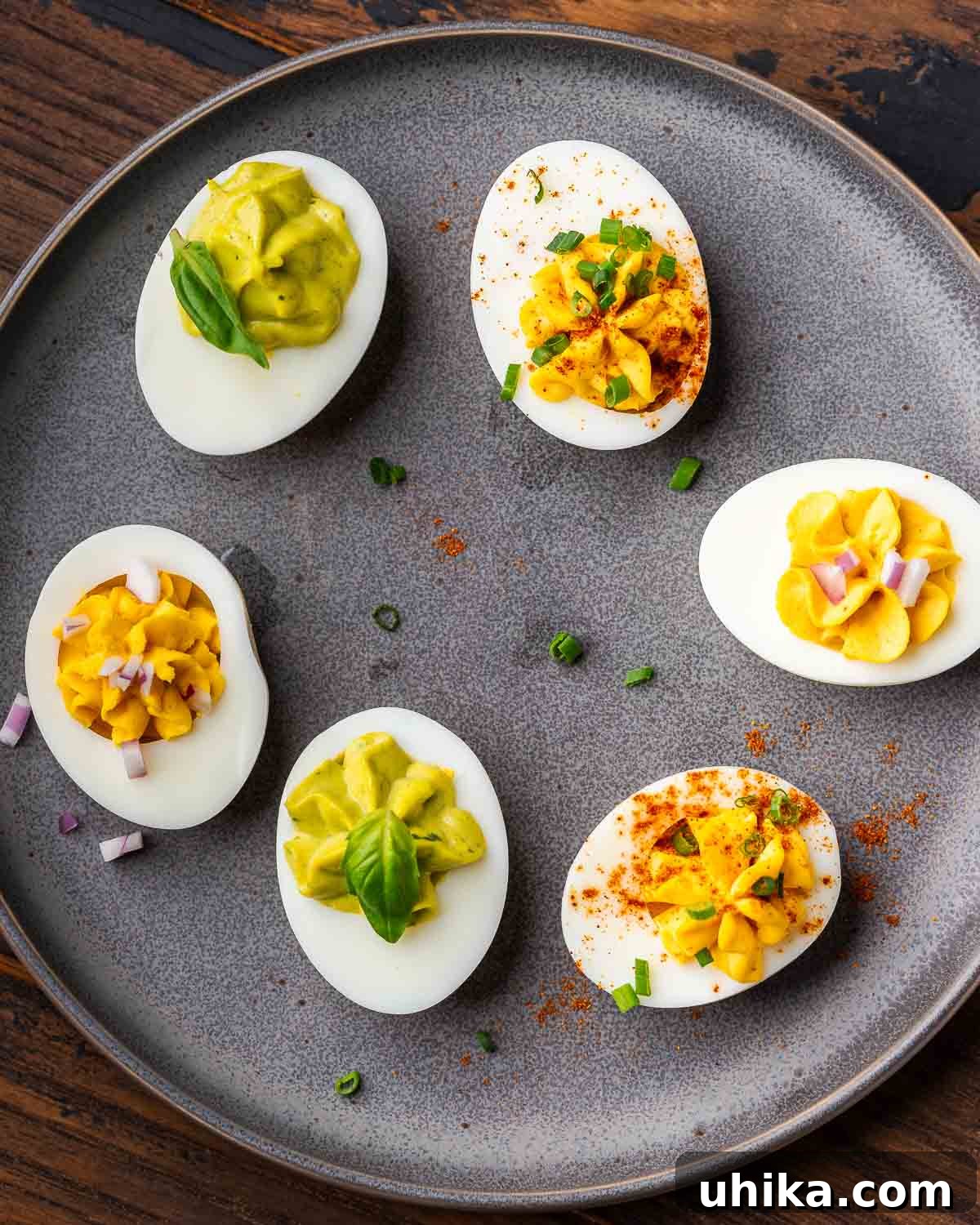Timeless Deviled Eggs 6 A vibrant display of deviled eggs featuring three distinct filling variations: classic, curried, and pesto-infused, presented neatly on a stylish grey plate.