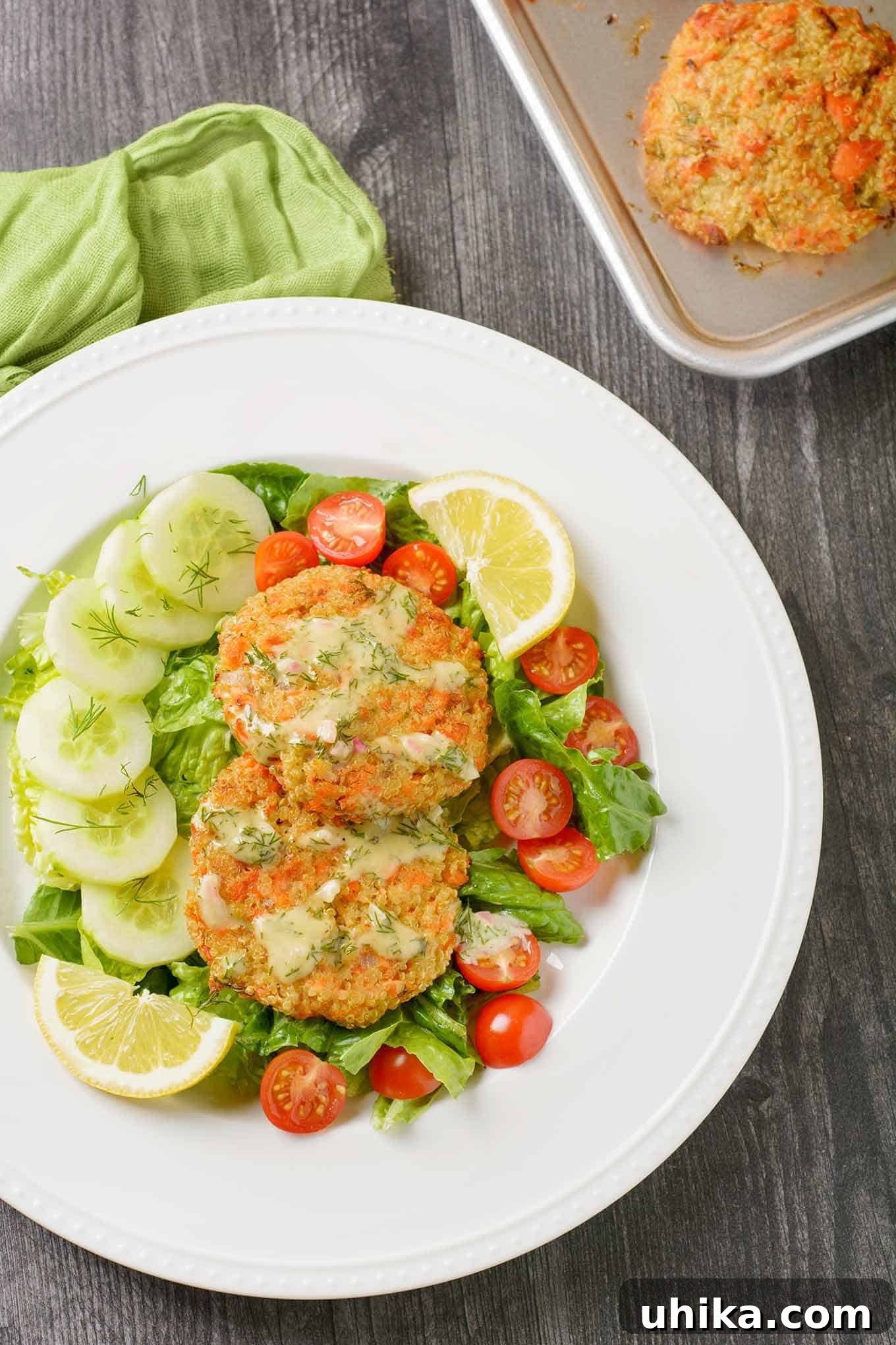 Savory Salmon Quinoa Cakes 2 A vibrant green salad featuring fresh lettuce, juicy cherry tomatoes, crisp cucumber slices, topped with bright lemon wedges, fresh dill, two perfectly baked salmon quinoa patties, and a drizzle of creamy dill dressing.