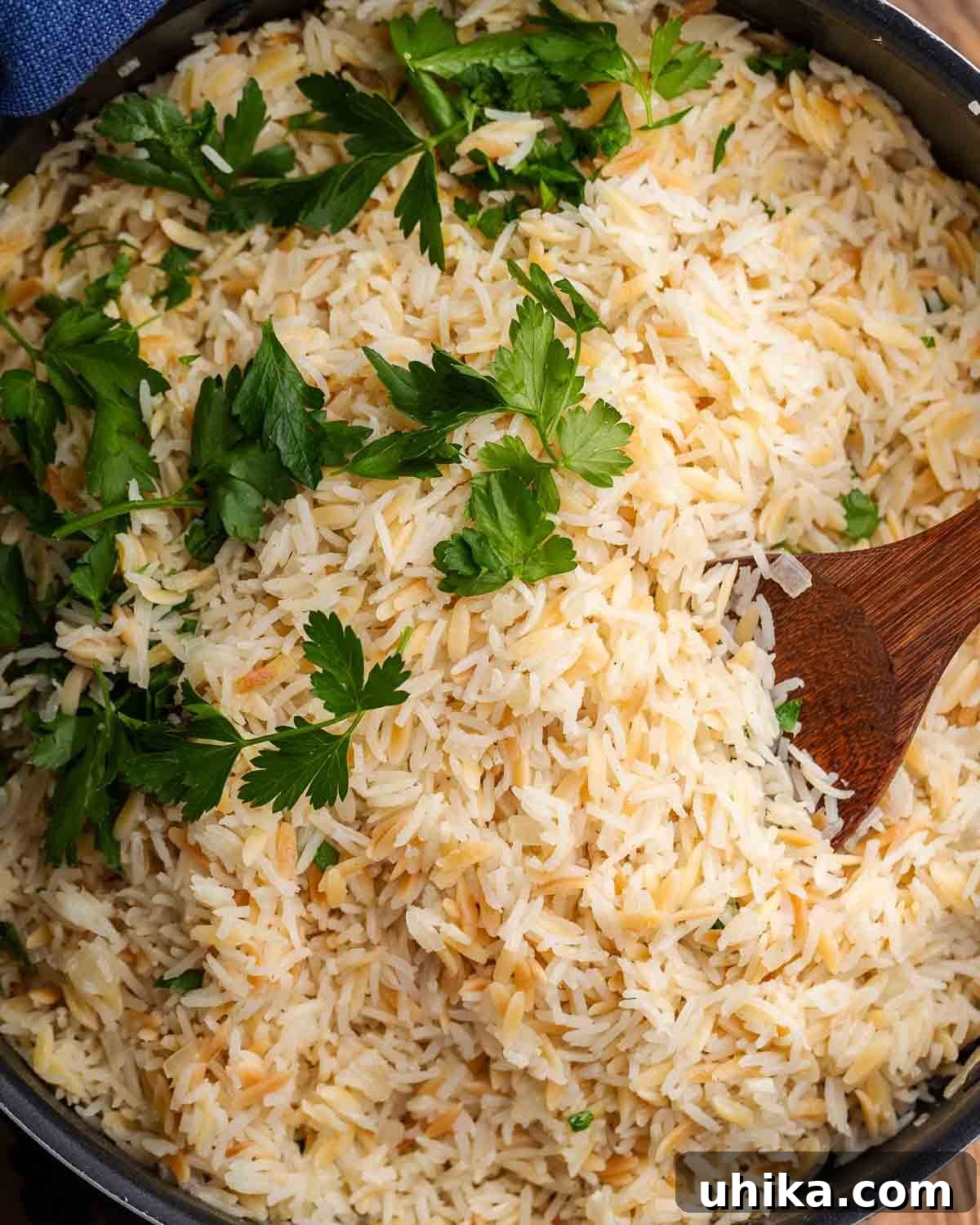 Aromatic Buttered Rice 2 Siyah bir tencerede maydanoz ve ceviz kaşıkla süslenmiş pirinç pilavı.