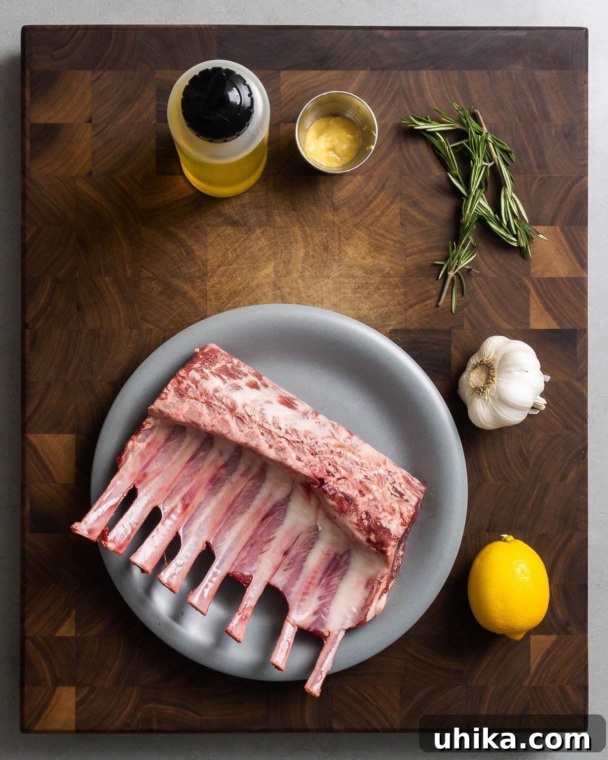 Chargrilled Lamb Rib Chops with Zesty Lemon Garlic 3 Ingredients shown: olive oil, Dijon mustard, rosemary, garlic, lemons, and rack of lamb.