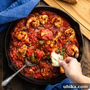 Large black pan with shrimp arrabbiata and hand dipping bread into the sauce.