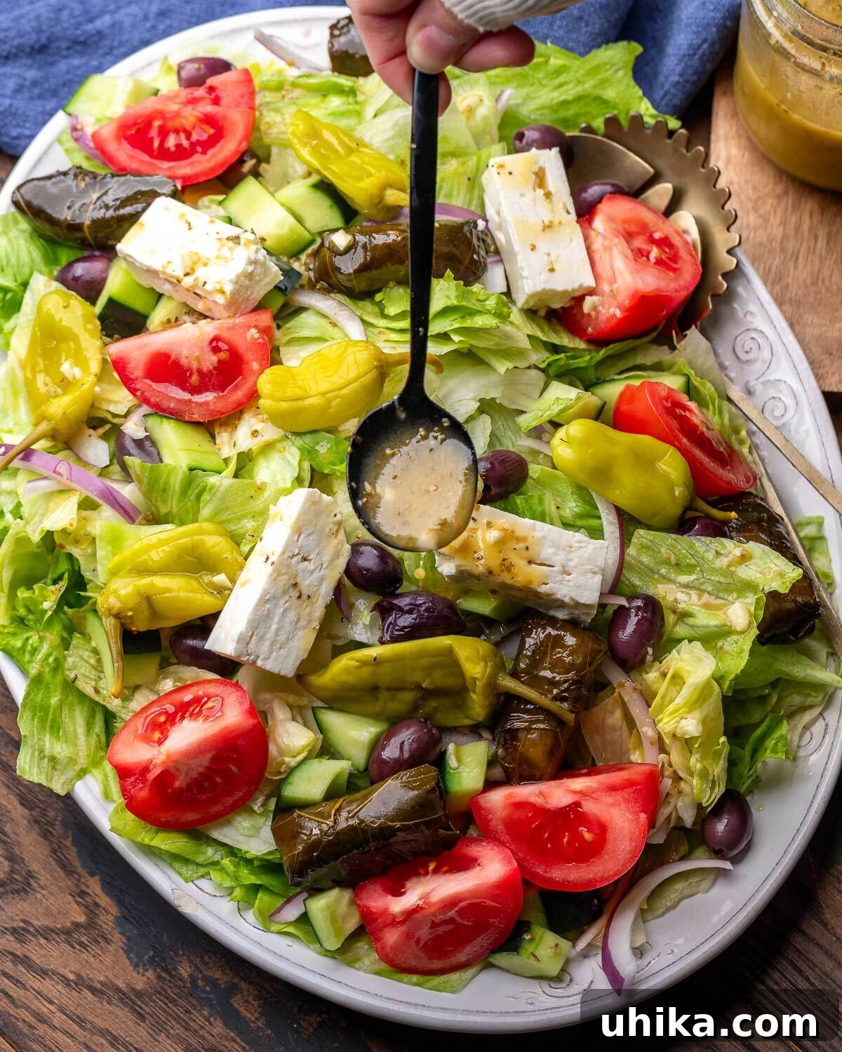 Classic New York Diner Greek Salad 2 Diner-style Greek salad in white platter with spoon drizzling Greek vinaigrette on top.