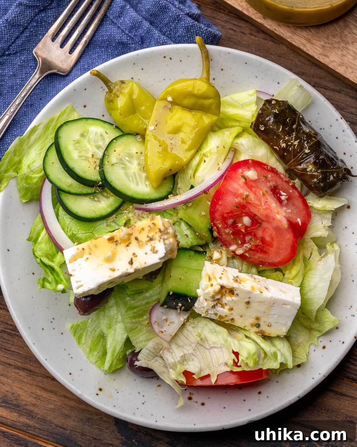 Classic New York Diner Greek Salad 4 White plate with Greek salad topped with feta cheese, Tuscan peppers, grape leaves, cucumbers, and tomatoes.