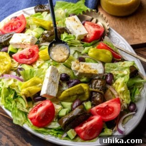 Diner Greek salad on large white platter with spoon drizzling Greek vinaigrette on top.