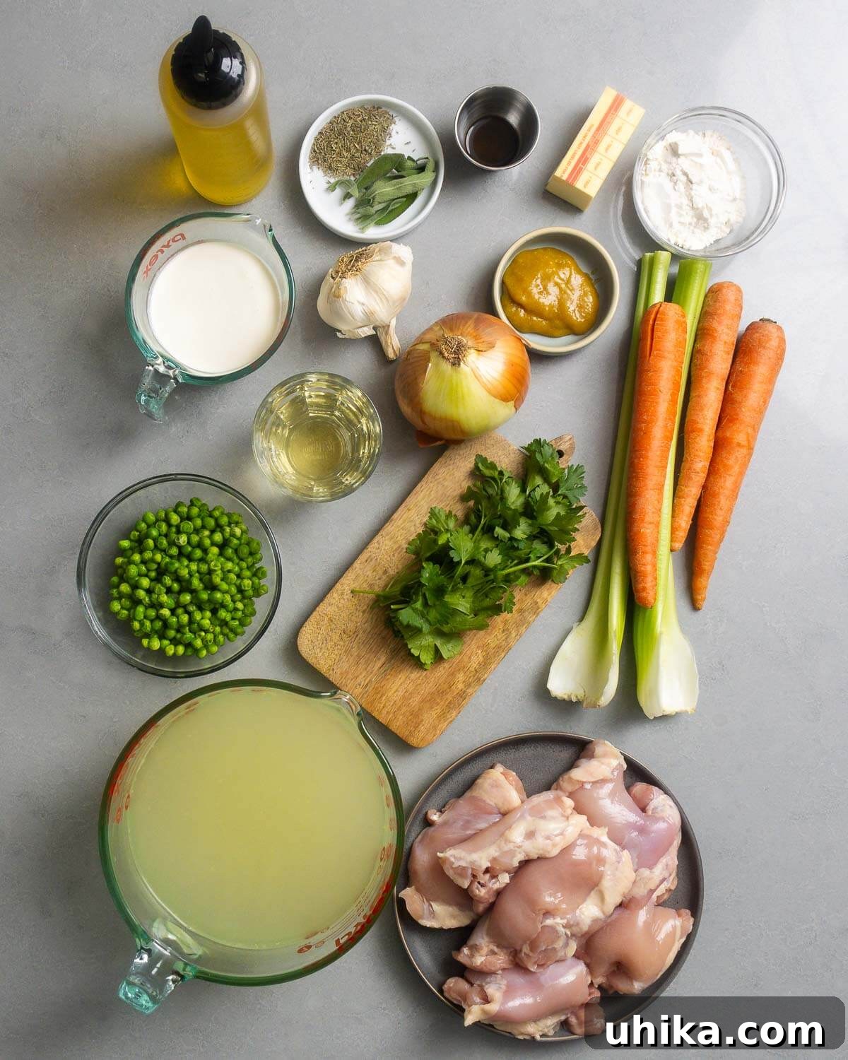 Hearty Homestyle Chicken and Dumplings 3 A vibrant display of fresh and pantry ingredients laid out for making the chicken and dumplings soup, including chicken thighs, olive oil, a selection of herbs, Worcestershire sauce, butter, flour, heavy cream, minced garlic, chicken base, diced onion, white wine, sliced celery, carrots, and frozen peas.