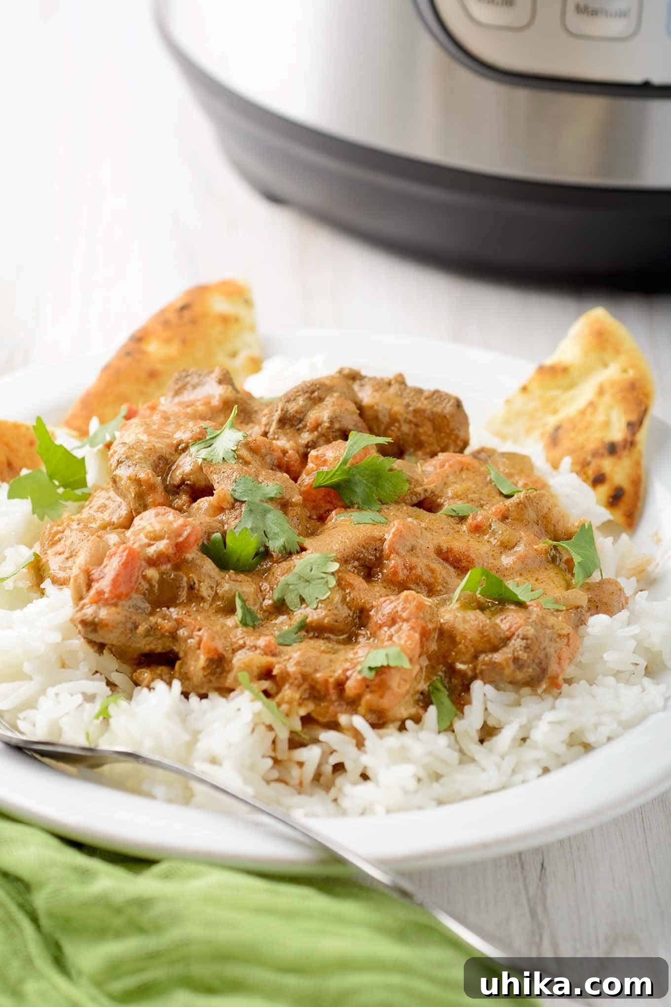 Effortlessly Delicious Instant Pot Chicken Tikka Masala 3 Chicken tikka masala over rice with naan, green napkin and fork in the foreground, Instant Pot in the background. A close-up of a delicious homemade Instant Pot Chicken Tikka Masala.