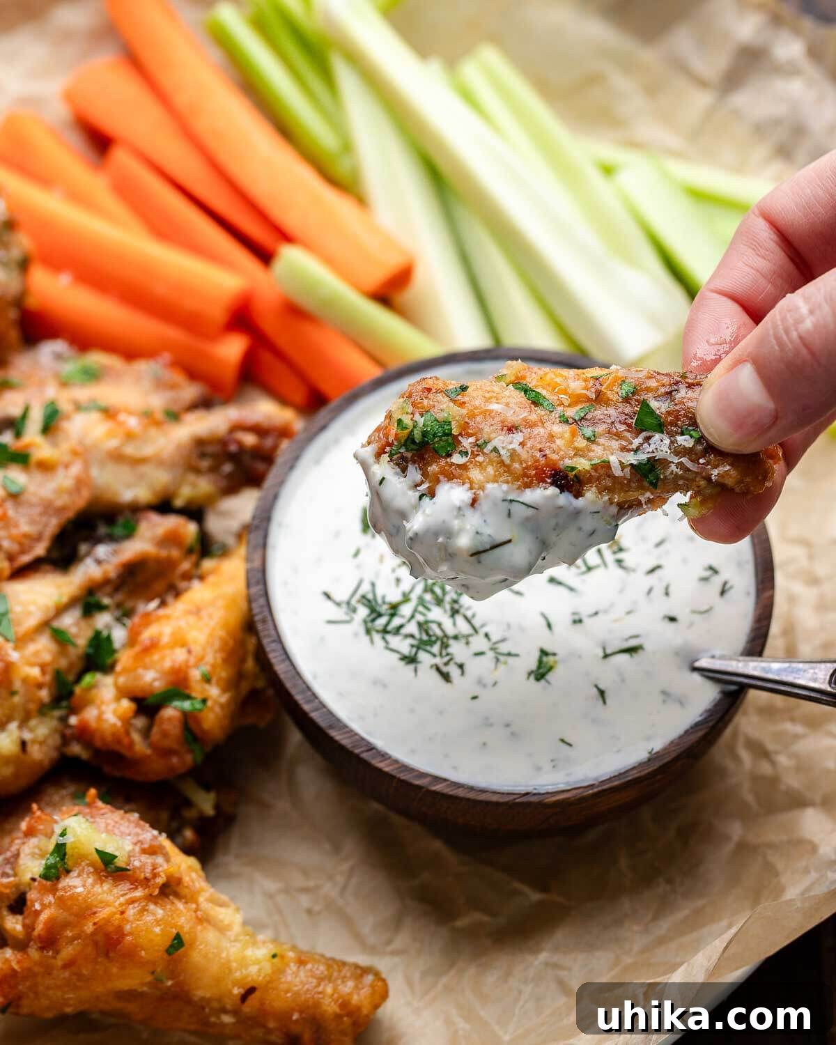 Irresistible Crispy Garlic Parmesan Wings 7 A hand dipping a crispy garlic parmesan chicken wing into a bowl of creamy ranch dressing.