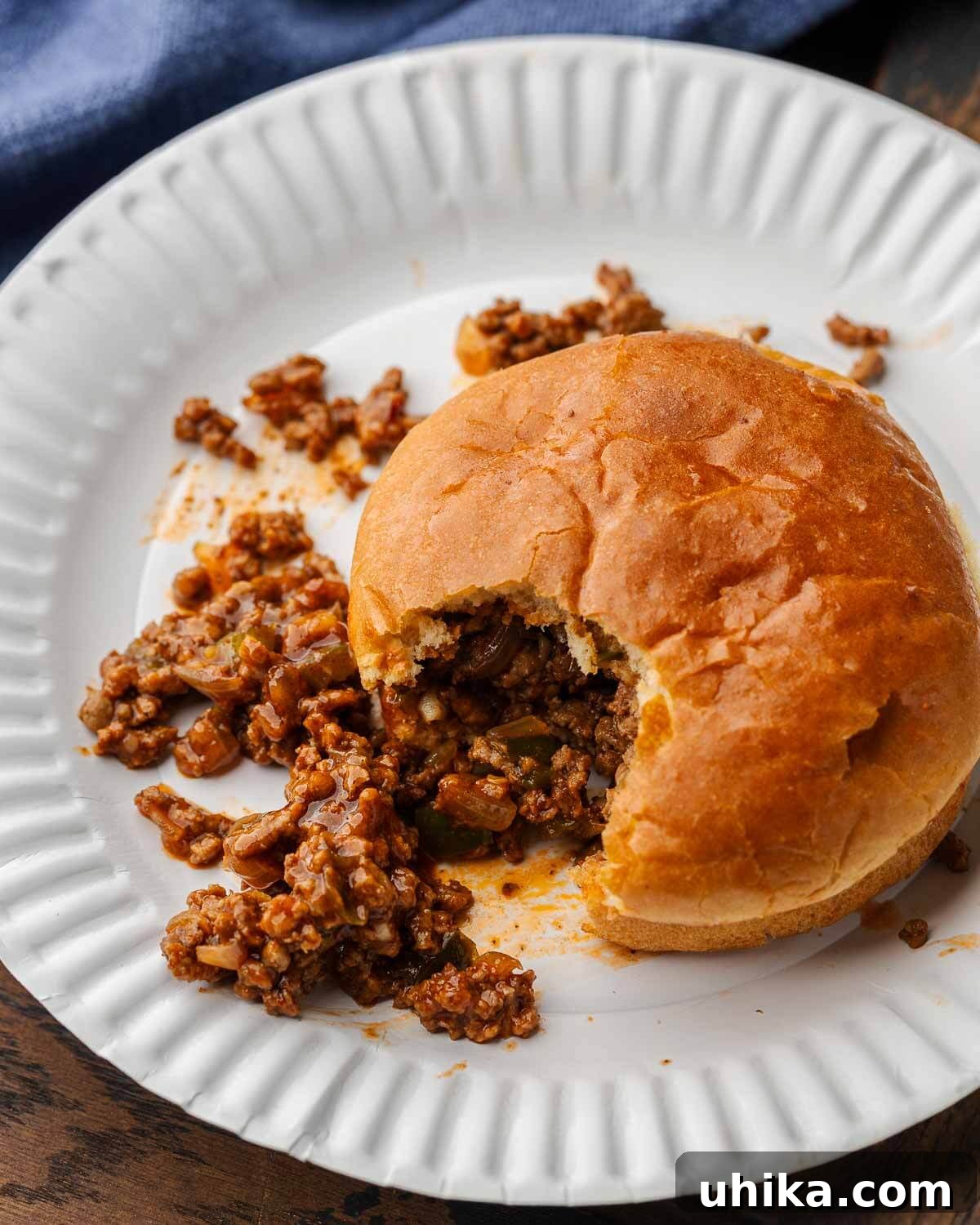 Effortless Homemade Sloppy Joes 7 Sloppy Joe sandwich with bite taken out of it on white paper plate, showcasing the rich filling.