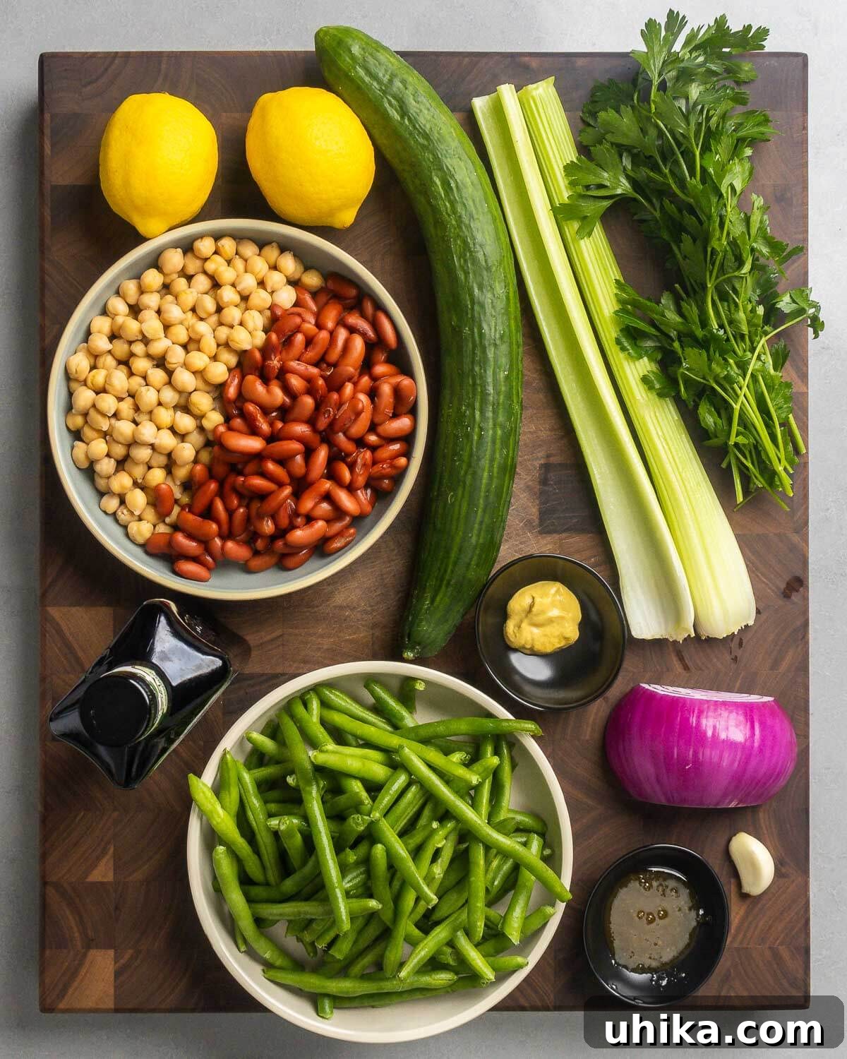 Zesty Mixed Bean Medley 3 A flat lay photograph showcasing all the fresh ingredients needed: lemons, cucumber, celery, parsley, chickpeas, olive oil, Dijon mustard, vibrant green beans, golden honey, red onion, and fresh garlic.
