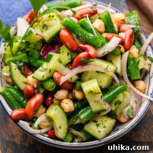 Mixed bean salad in white and blue bowl topped with parsley and red onions.