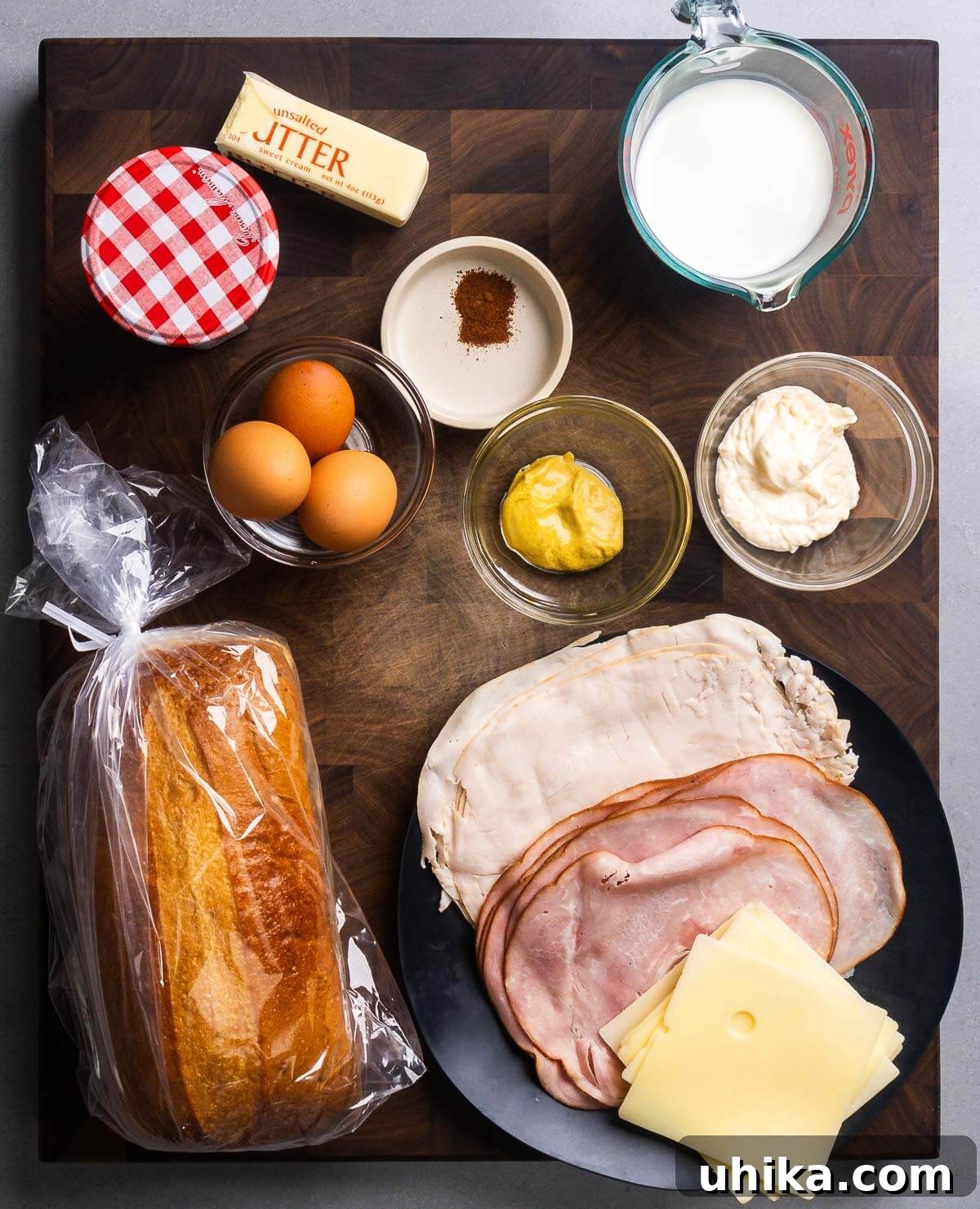 Monte Cristo's Reckoning 3 A flat lay photograph showcasing all the ingredients required for a Monte Cristo sandwich: raspberry jam, butter, nutmeg, milk, eggs, Dijon mustard, mayonnaise, slices of white bread, deli-sliced turkey, honey ham, and Swiss cheese.