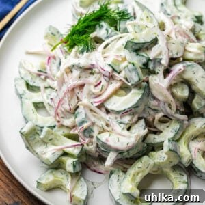 Creamy cucumber salad on white plate with dill garnish.