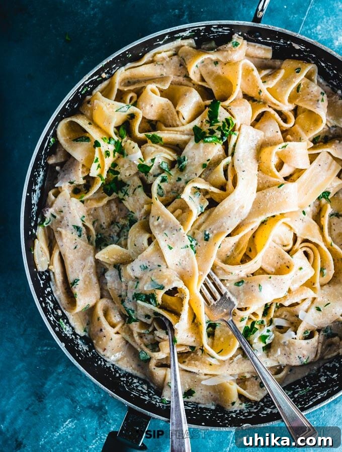 Walnut sauce being mixed with cooked pasta in a large pan.