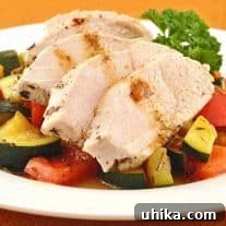 Sliced herb and butter poached chicken breast served over a medley of sautéed zucchini and red bell peppers, garnished with parsley on a white plate.