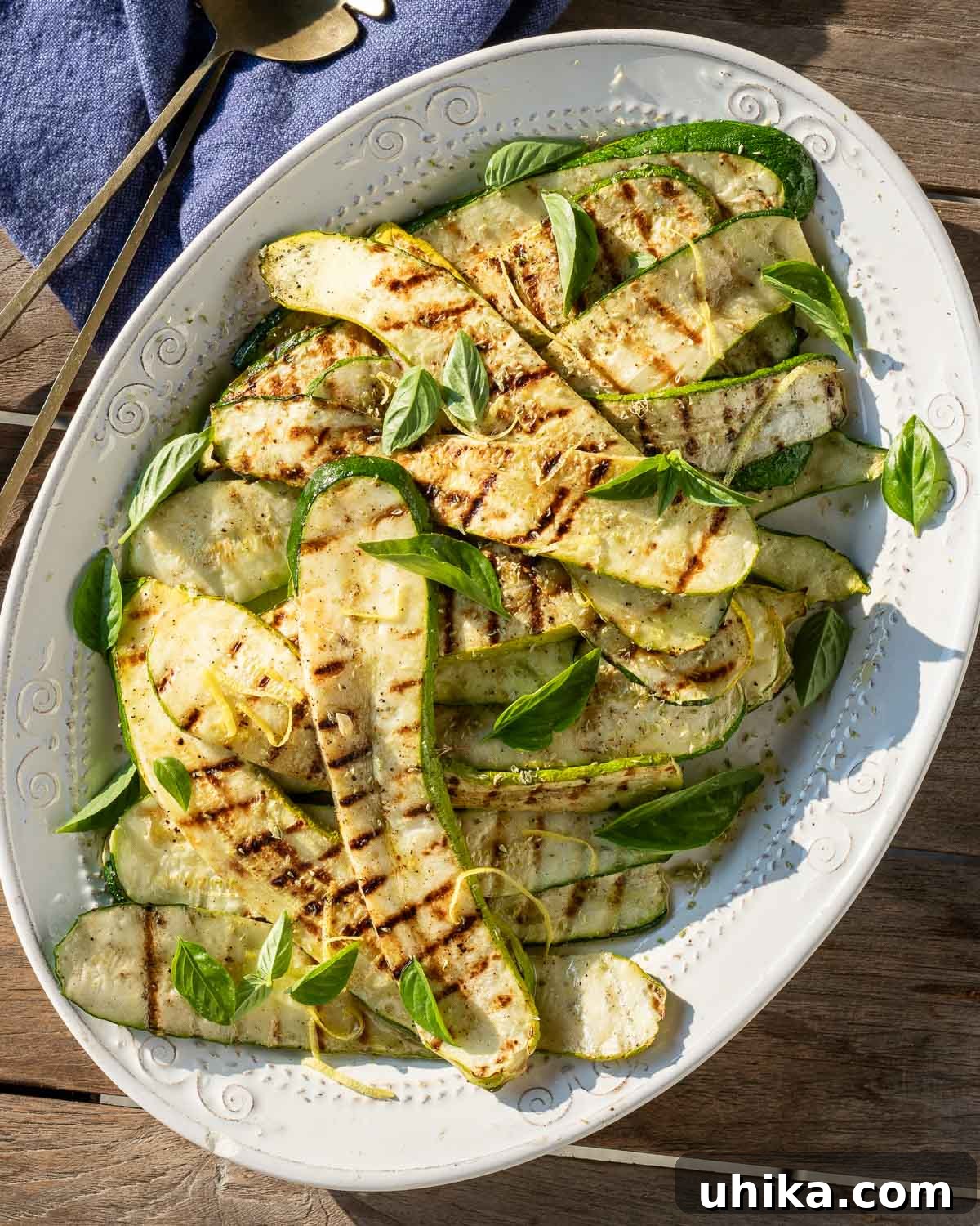 Garlic Herb Grilled Zucchini 2 Perfectly grilled zucchini slices arranged on a pristine white platter, garnished with fresh herbs and lemon wedges.