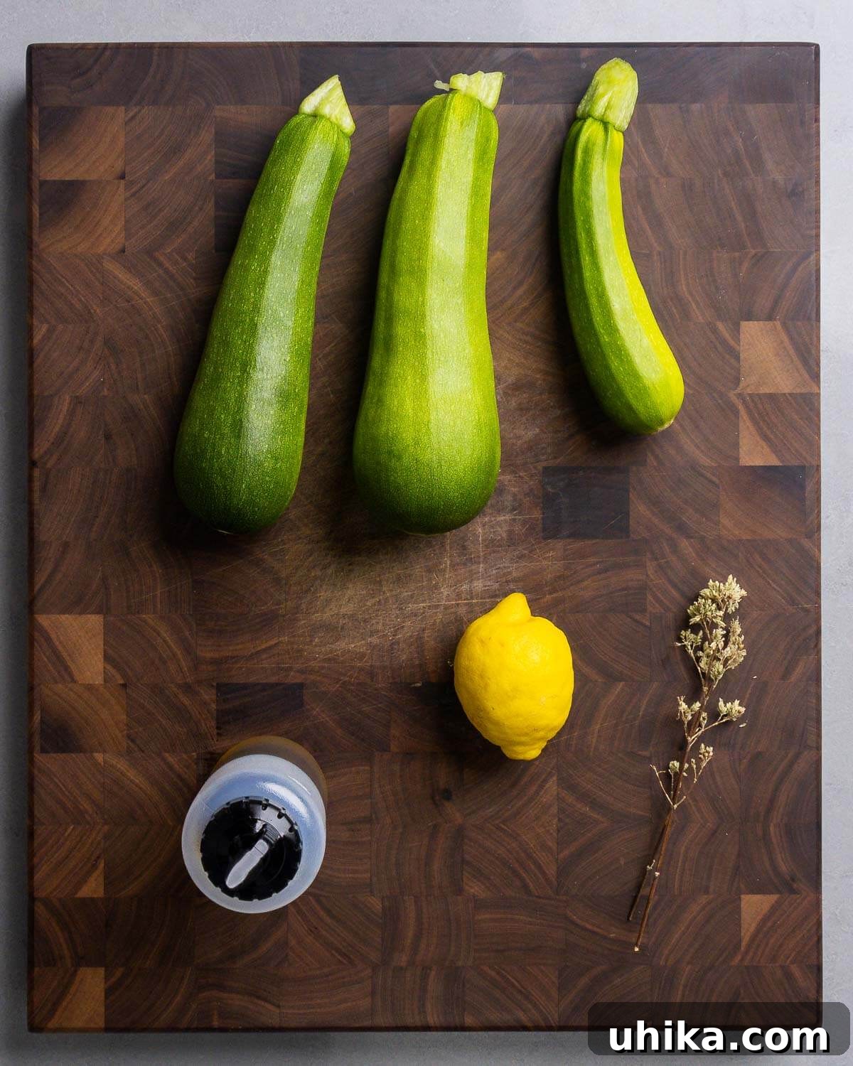 Garlic Herb Grilled Zucchini 3 A selection of fresh ingredients including zucchini, a bottle of olive oil, a whole lemon, and a small bowl of dried Sicilian oregano.