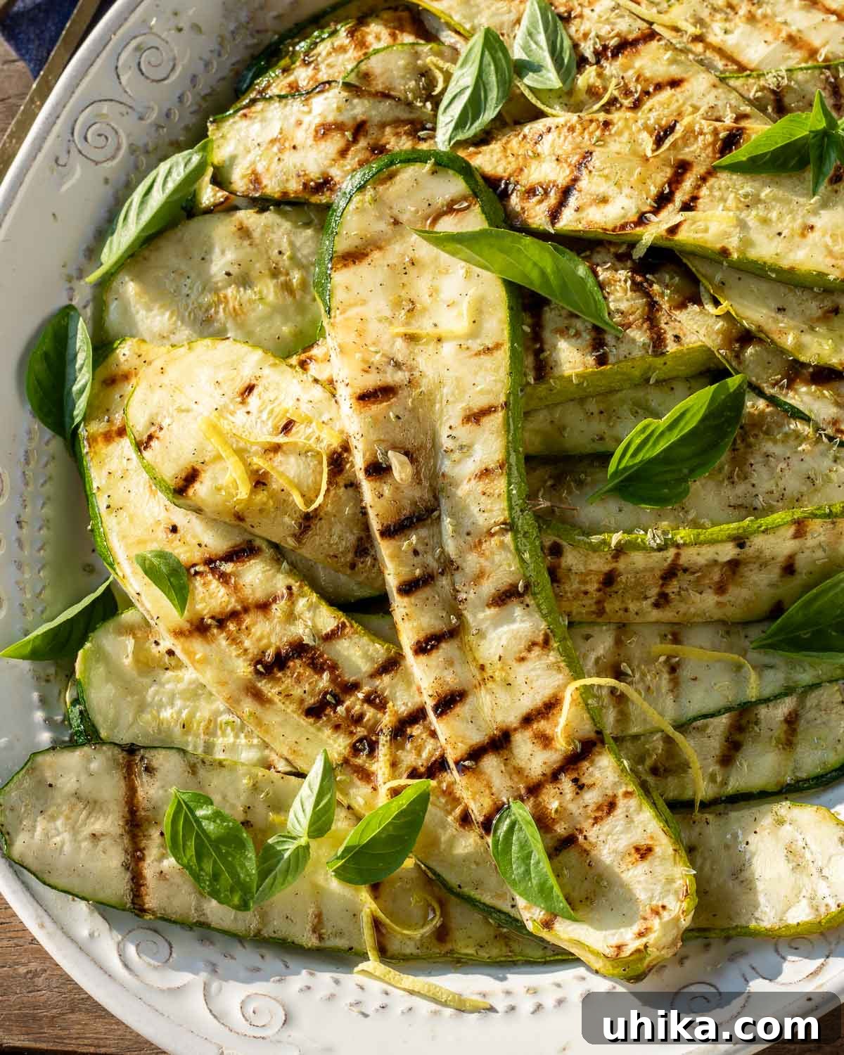 Garlic Herb Grilled Zucchini 5 Grilled zucchini garnished with fresh basil leaves on a white platter, ready for serving.