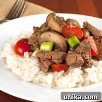 Tenderloin beef tips sautéed with mushrooms, cherry tomatoes, and scallions served over a bed of white rice on a white plate.