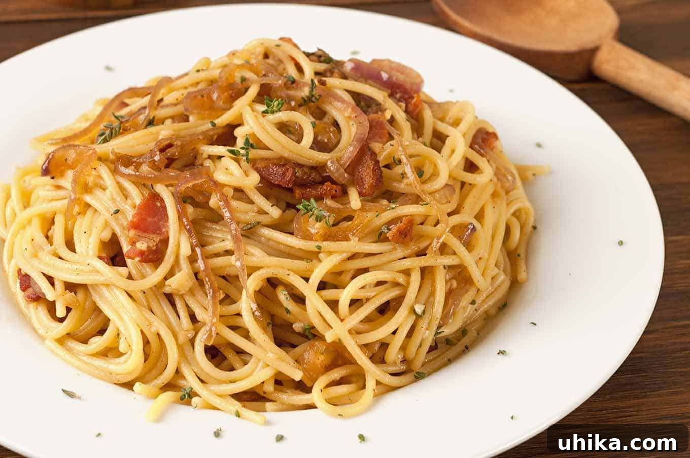 Aromatic Thyme, Bacon, and Onion Spaghetti 3 A close-up of a plate of spaghetti tossed with crispy bacon, caramelized onions, and fresh thyme on a white dish.