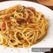 A plate of spaghetti tossed with crispy bacon, caramelized onions, and fresh thyme on a white dish.