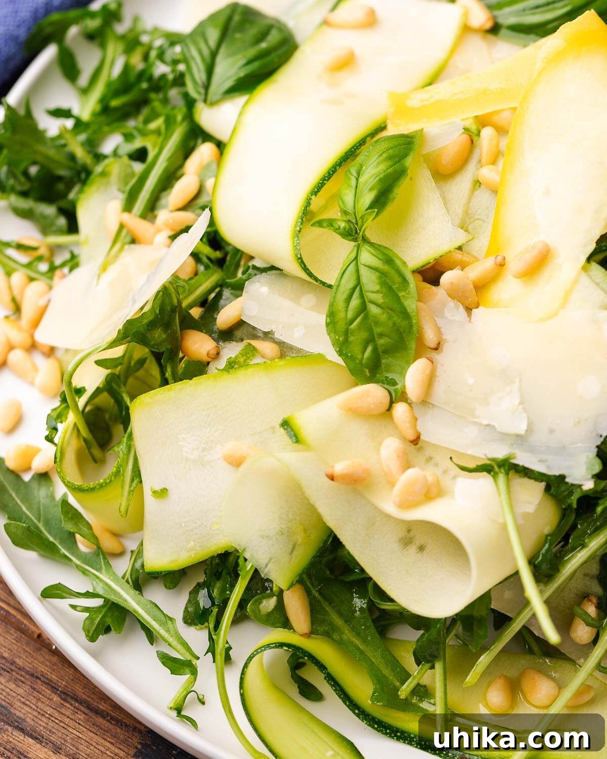 Refreshing Zucchini Ribbons Salad 2 Closeup shot of ribbons of shaved zucchini, basil, and pine nuts salad on white platter.