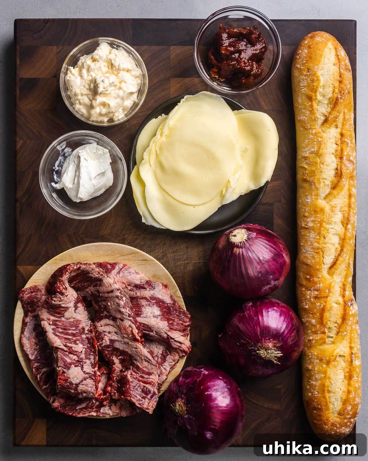 The Ultimate Steak Sandwich 3 Ingredients for a steak sandwich recipe laid out: mayonnaise, chipotles in adobo sauce, sour cream, provolone cheese, baguette, skirt steak, and red onions.
