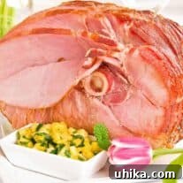 Pineapple Mint Chutney Glazed Ham 3 A close-up of a spiral-sliced, glazed, baked ham on a serving platter with an accompanying bowl of pineapple mint chutney.