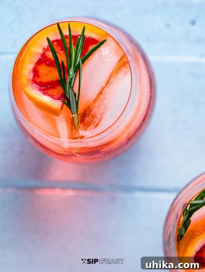 Aperol Spritz - Garnish with Orange and Rosemary A single Aperol Spritz cocktail in a wine glass, garnished with a vibrant orange slice and a sprig of fresh rosemary, resting on ice.