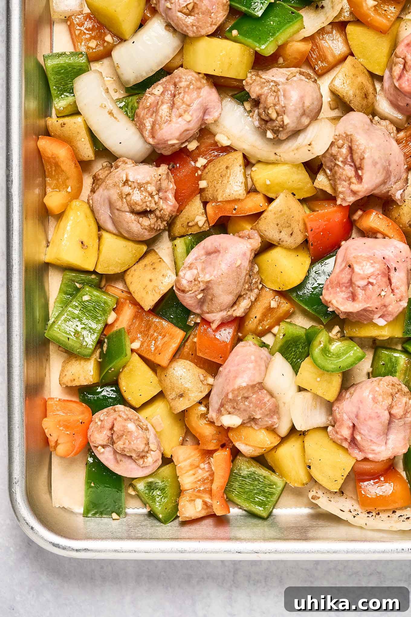 Par-baked bell peppers and baby yellow potatoes topped with chunks of Italian sausage on top, ready to continue cooking.