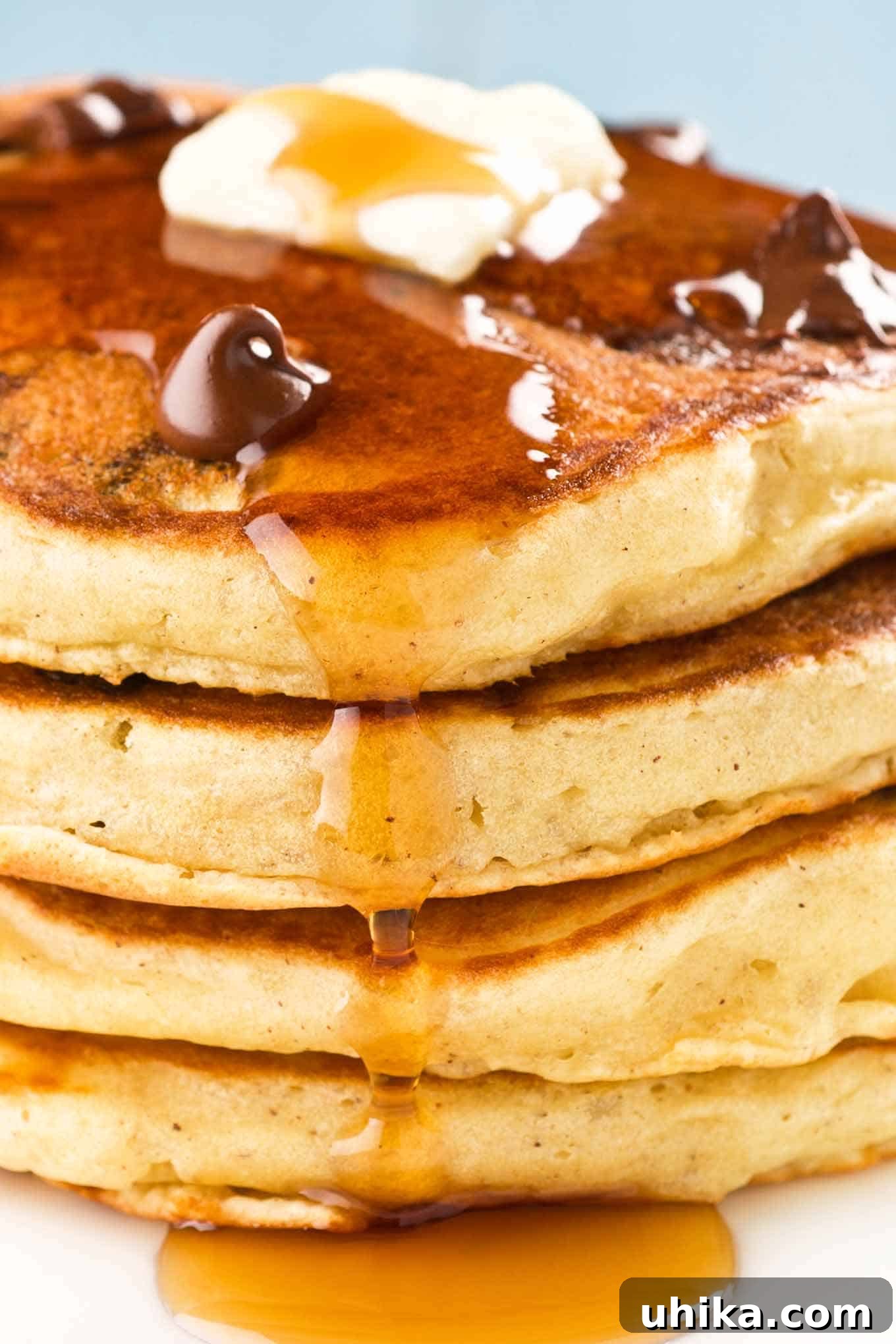 Decadent Chocolate Chip Pancakes with Maple-Glazed Bacon 2 A close view of a stack of fluffy chocolate chip and candied bacon pancakes, topped with melting butter, extra chocolate chips, and maple syrup.