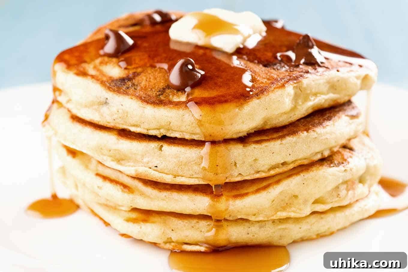 Decadent Chocolate Chip Pancakes with Maple-Glazed Bacon 3 A stack of four chocolate chip and candied bacon pancakes topped with a few extra chocolate chips, a pat of butter, and a drizzle of maple syrup.