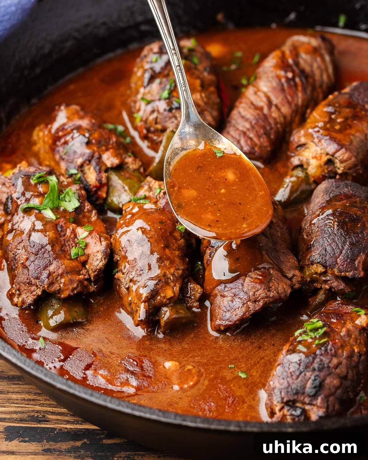 Hearty German Beef Rouladen 2 Spoon pouring sauce over beef rouladen in cast iron pan.