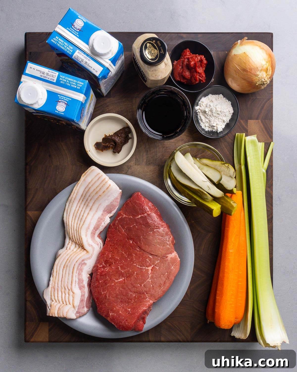 Hearty German Beef Rouladen 3 Ingredients shown: boxed beef stock, mustard, tomato paste, flour, onion, beef base, red wine, pickles, carrots, celery, bacon, and top round.