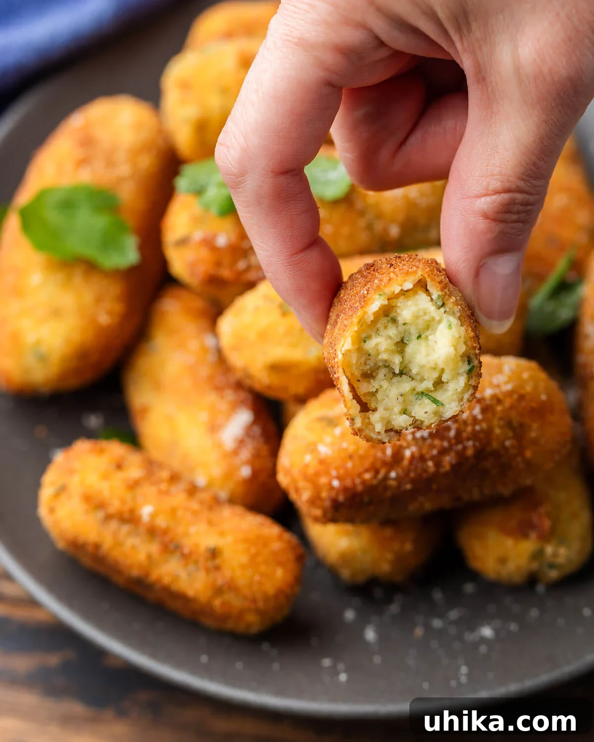 Crispy Italian Potato Bites 6 A hand holding a perfectly fried Italian potato croquette that has been bitten into, revealing its fluffy interior.