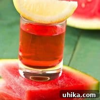 A Watermelon Drop shot in a small glass, featuring a vibrant pink liquid and garnished with a crisp lemon wedge, ready to be enjoyed.
