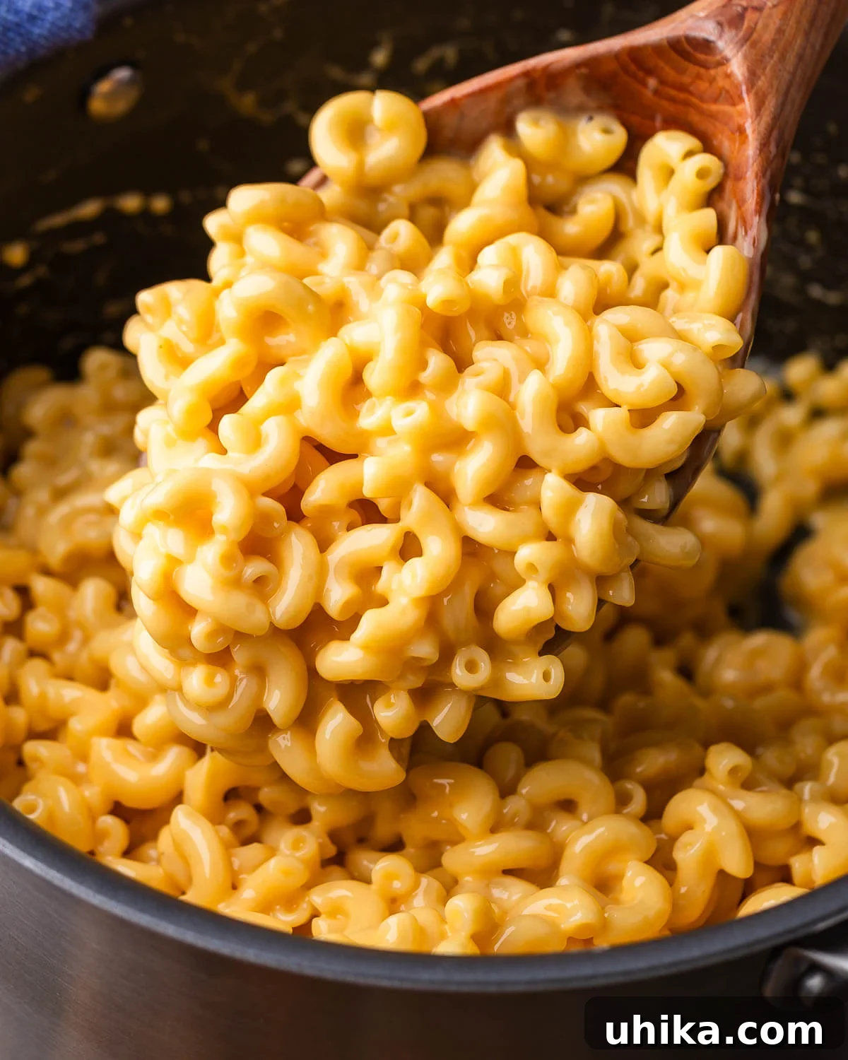 Large wooden ladle holding a generous serving of creamy stovetop mac and cheese, showcasing its rich texture and golden color.