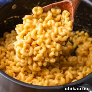 Large ladle spooning elbow mac and cheese over pot, highlighting the creamy texture.