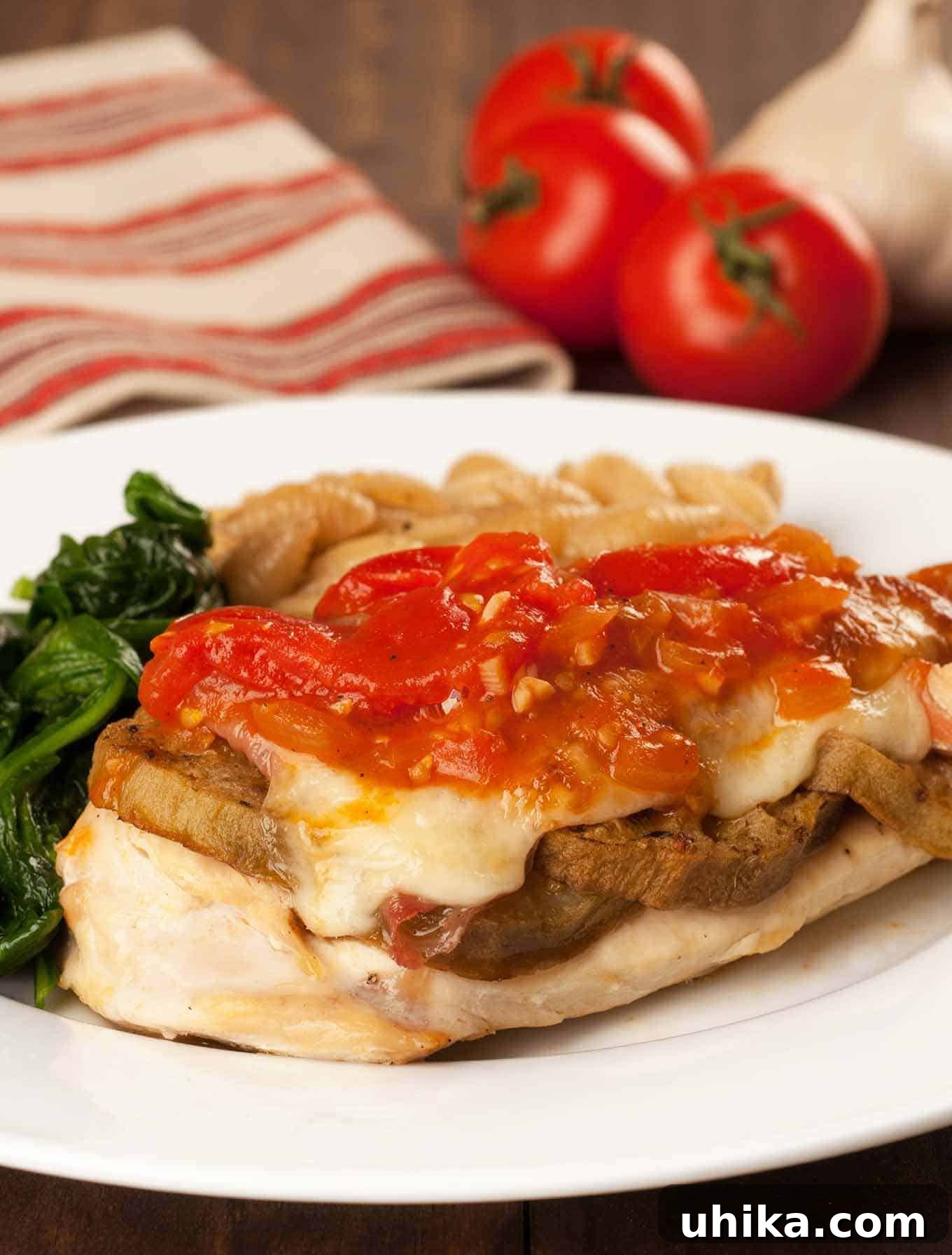 Neapolitan Chicken Layers 2 Exquisite plate of Chicken Sorrentino, featuring golden-brown chicken breast topped with tender roasted eggplant, savory prosciutto, and melted provolone cheese, generously drizzled with a rich tomato-marsala cream sauce. Served alongside vibrant sautéed spinach and delicate pasta shells, ready to be enjoyed.