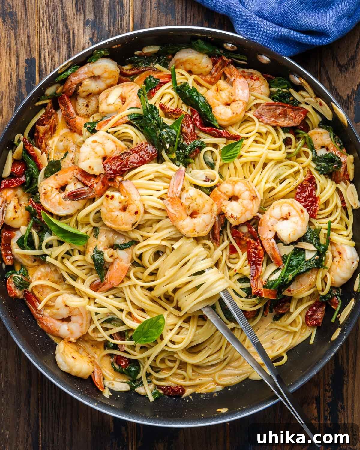 Sunset Shrimp Pasta 6 Overhead shot of creamy sun dried tomato shrimp pasta in black pan with kitchen tweezers.