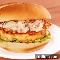 Delicious Salmon Burgers with Tangy Sun Dried Tomato Aioli 3 A grilled salmon burger topped with sun-dried tomato and chive mayonnaise on a lettuce-lined bun, served on a white plate.